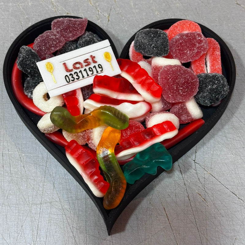 Black 3D-printed heart-shaped candy container filled with a variety of colorful gummy worms and gummy bears  .