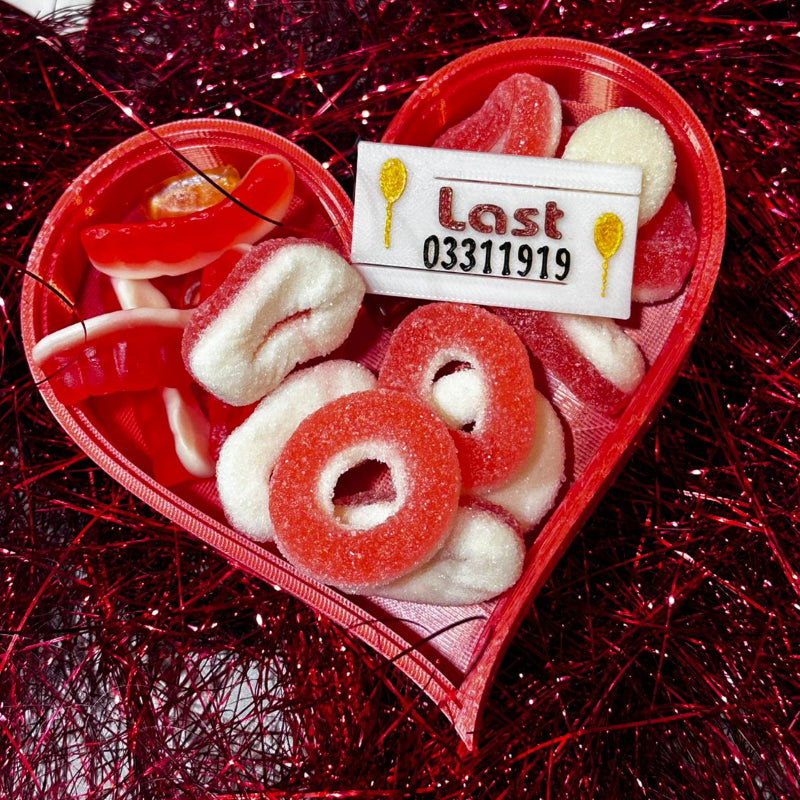 Red 3D-printed heart-shaped candy dish filled with red and white sugar-coated gummy rings and sweets .