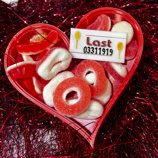 Red 3D-printed heart-shaped candy dish filled with red and white sugar-coated gummy rings and sweets .
